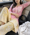 A woman seated in a beige car interior wearing a pink and pale yellow premium chikankari embroidered traditional outfit with white floral lace detailing. wearing chikankari kurti for women 