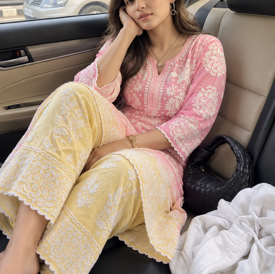 A woman seated in a beige car interior wearing a pink and pale yellow premium chikankari embroidered traditional outfit with white floral lace detailing. wearing chikankari kurti for women 