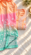 A peach and mint green gradient embroidered kurta set with white floral embroidery, styled on a white faux fur surface with dappled sunlight.