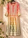 A long kurta dress hanging on a black hanger against a sunlit beige wall, featuring a vertical gradient from coral pink at the top to golden yellow in the middle and sage green at the bottom, with extensive cream floral embroidery. Decorative text on the right reads 'Candy PURE HANDCRAFTED chikankari kurta'.